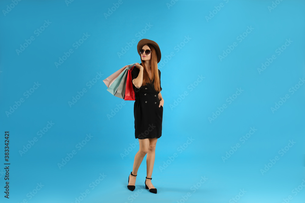 Beautiful young woman with paper shopping bags on light blue background Beautiful young woman with paper shopping bags on light blue background