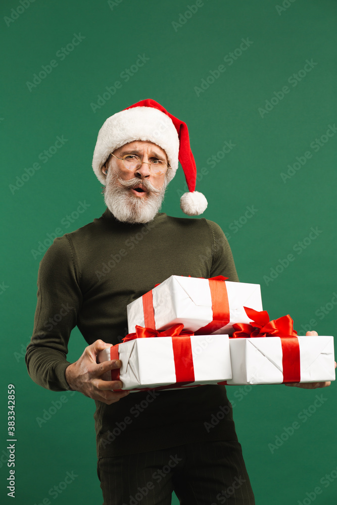 Bearded modern Santa Claus holding gifts and smiling on the green background Bearded modern Santa Claus holding gifts and smiling on the green background