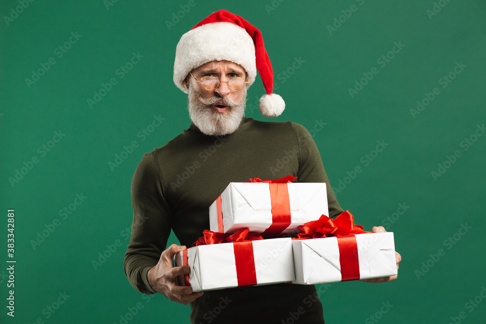 Bearded modern Santa Claus holding gifts and smiling on the green background Bearded modern Santa Claus holding gifts and smiling on the green background