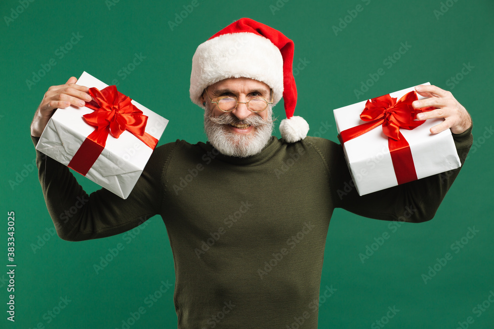 Bearded modern Santa Claus holding gifts and smiling on the green background Bearded modern Santa Claus holding gifts and smiling on the green background