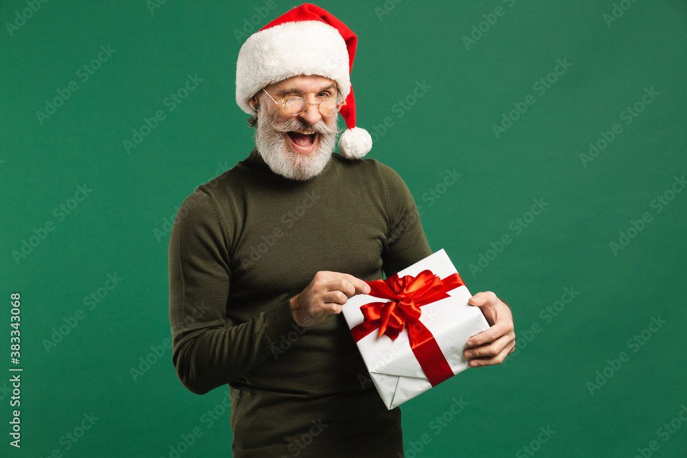 Happy bearded modern Santa Claus holding gift and joking on the green background Happy bearded modern Santa Claus holding gift and joking on the green background