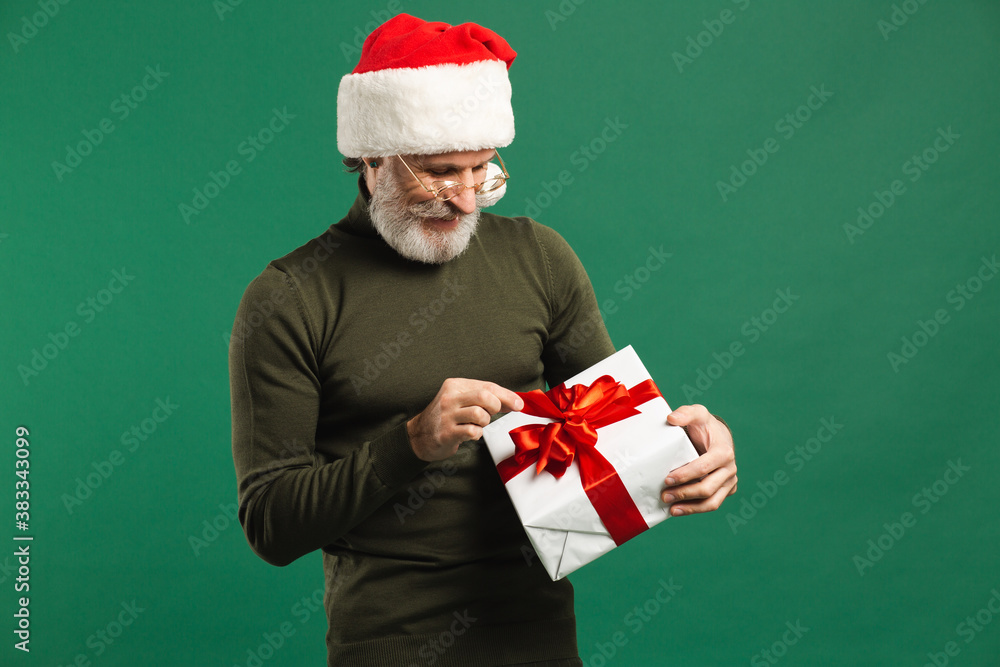 Happy bearded modern Santa Claus holding gift and joking on the green background Happy bearded modern Santa Claus holding gift and joking on the green background