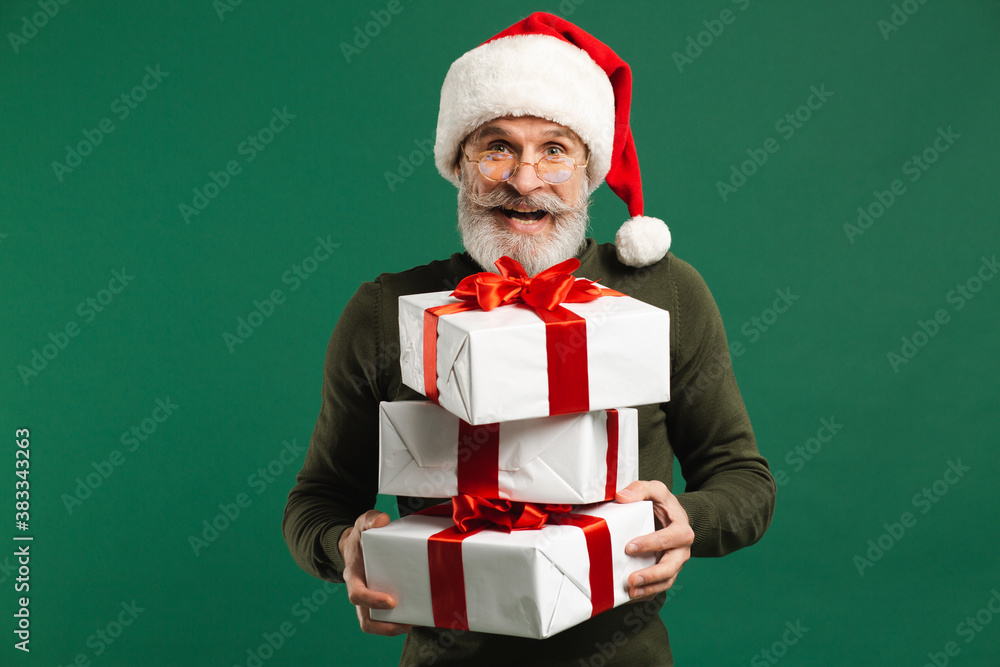 Bearded modern Santa Claus holding gifts and smiling on the green background Bearded modern Santa Claus holding gifts and smiling on the green background