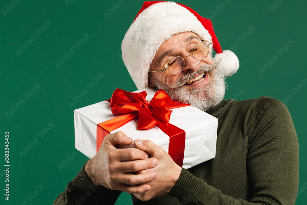 Happy bearded modern Santa Claus hugging gift on the green background Happy bearded modern Santa Claus hugging gift on the green background