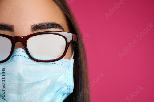 Young woman with foggy glasses caused by wearing disposable mask on pink background, space for text. Protective measure during coronavirus pandemic