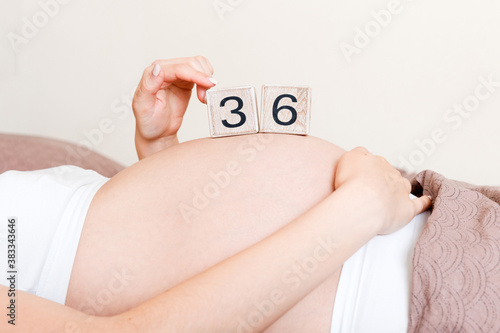 Pregnant woman in white underwear on bed in home holding calendar with weeks 36 of pregnant. Maternity concept. Expecting an upcoming baby © sosiukin