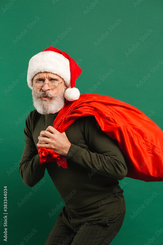 Happy bearded modern Santa Claus holding red bag on the green background Happy bearded modern Santa Claus holding red bag on the green background