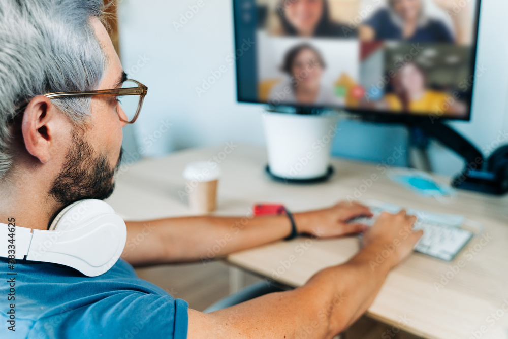 Obraz premium Back view of student with headphones having a video call at home during coronavirus outbreak - Young people having fun chatting online - Technology and friendship concept - Focus on man's head