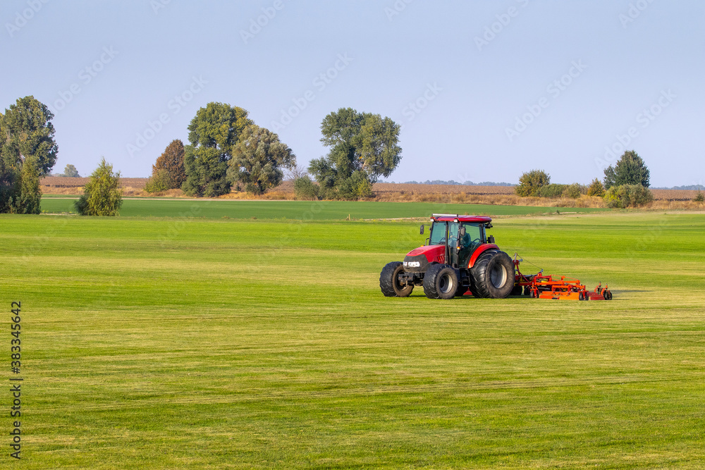 Industrial production of lawn grass in rolls. Trimmed field, resistant to mechanical impact and drought of green lawn grass. A tractor with a mower goes through the field, mows and mulches the grass. Industrial production of lawn grass in rolls. Trimmed field, resistant to mechanical impact and drought of green lawn grass. A tractor with a mower goes through the field, mows and mulches the grass.