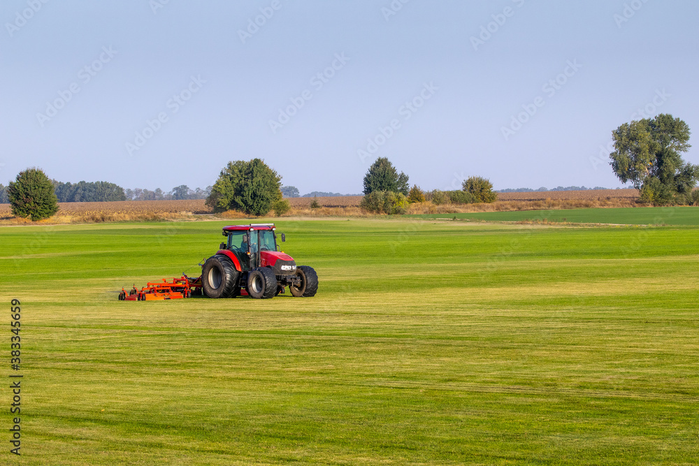 Industrial production of lawn grass in rolls. Trimmed field, resistant to mechanical impact and drought of green lawn grass. A tractor with a mower goes through the field, mows and mulches the grass. Industrial production of lawn grass in rolls. Trimmed field, resistant to mechanical impact and drought of green lawn grass. A tractor with a mower goes through the field, mows and mulches the grass.