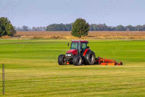 Industrial production of lawn grass in rolls. Trimmed field  resistant to mechanical impact and drought of green lawn grass. A tractor with a mower goes through the field  mows and mulches the grass.