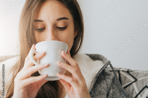 Close Up of Young Woman wearing sweater sipping coffee or tea from white mug in the morning photo