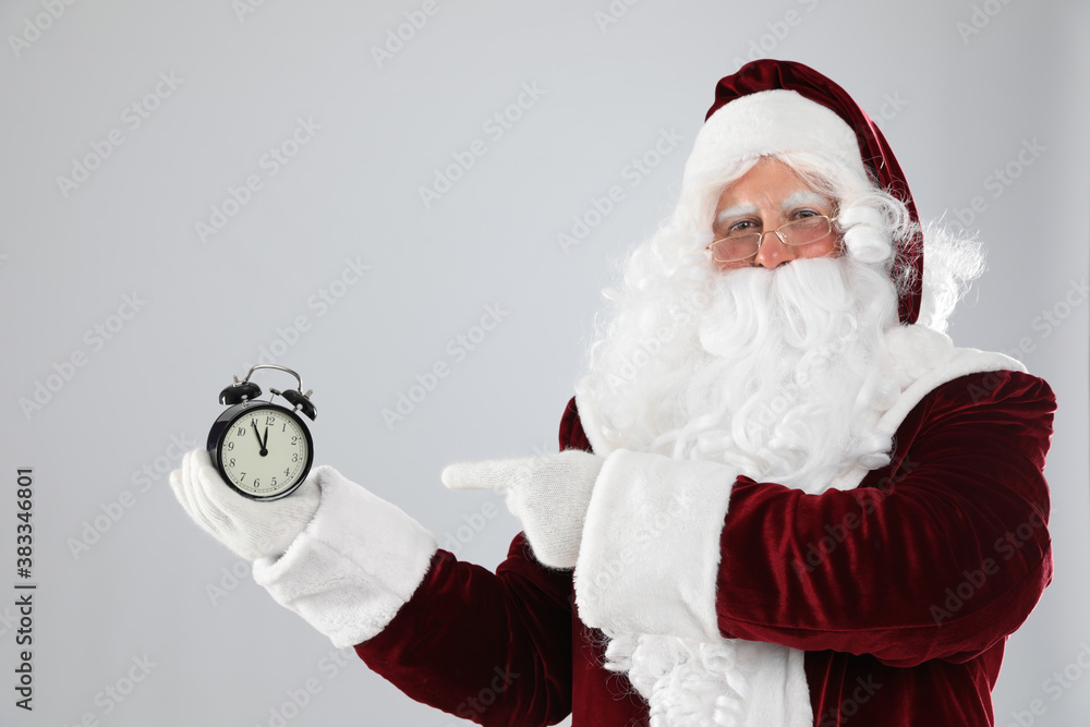 Santa Claus holding alarm clock on light grey background. Christmas countdown