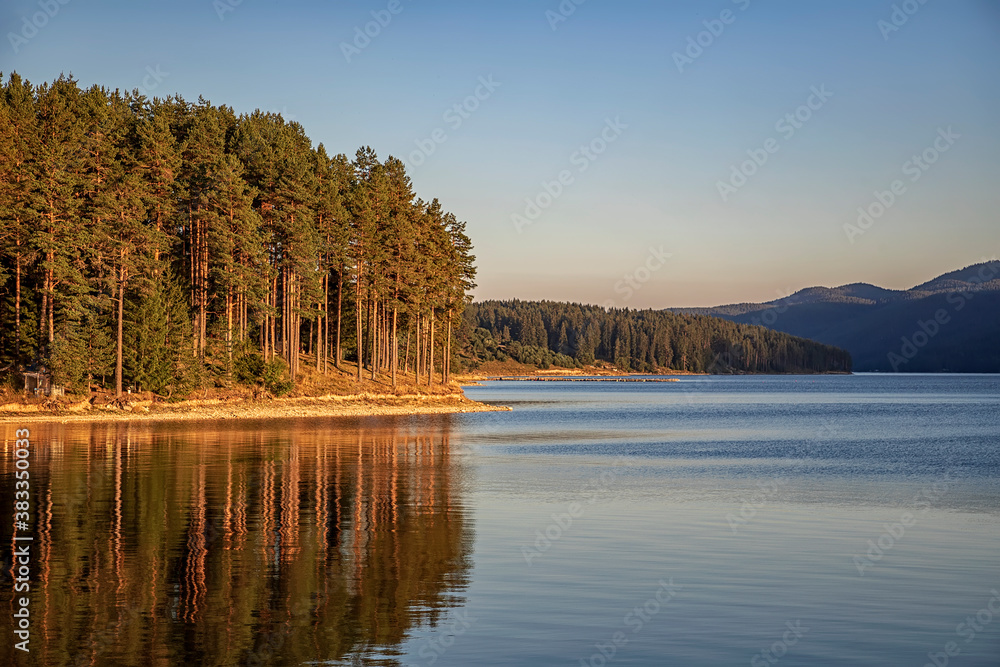 Idyllic mountain landscape at lake with calm water, tree reflection after sunset