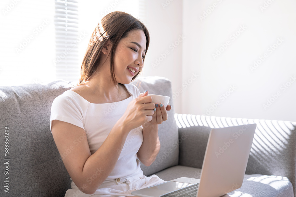 Beautiful young Asian woman working on laptop computer at the living room, Drinking coffee, Work from home. Beautiful young Asian woman working on laptop computer at the living room, Drinking coffee, Work from home.