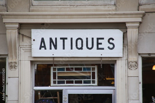 A wood board painted white with the word Antiques in black type.
