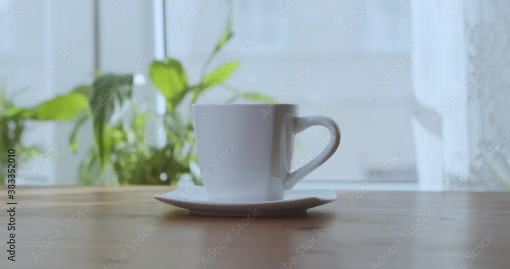 Woman's hand takes a mug of aromatic coffee on a wooden table in the room. Woman's hand takes a mug of aromatic coffee on a wooden table in the room.