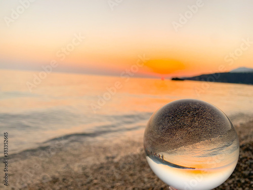 Beautiful sunset view through lens of crystal ball on water horizon © Xhemile