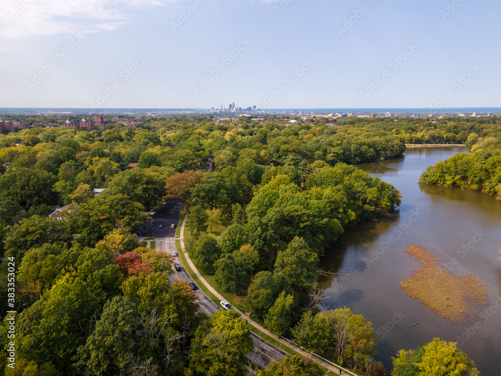 Fototapeta premium Roads and small lake in trees. Trees are changing for fall. Cleveland downtown in the far background