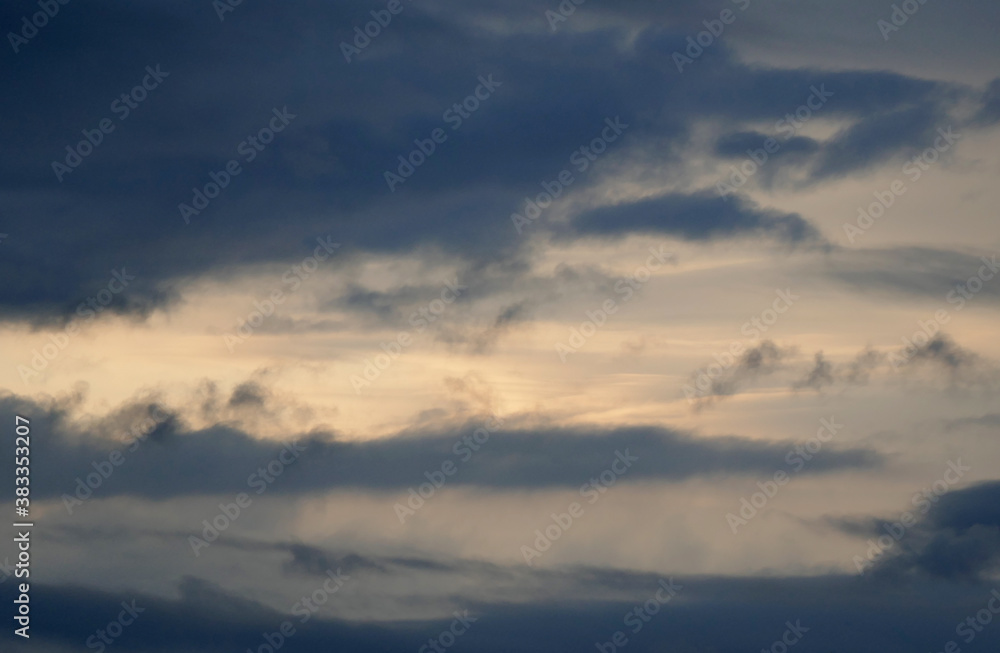 The evening sun shines easily through a dark cloud cover, orange sunshine, grey clouds in the sky The evening sun shines easily through a dark cloud cover, orange sunshine, grey clouds in the sky