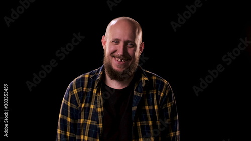 Bald bearded man in checkered shirt looks intently and angrily at the camera on black background. guy smiles and we see that he is missing one front tooth. Funny homeless man on the street at night.