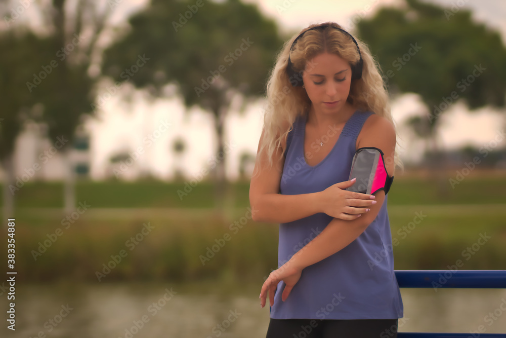 Young blonde woman starting application on a smartphone for running with headset. Young blonde woman starting application on a smartphone for running with headset.