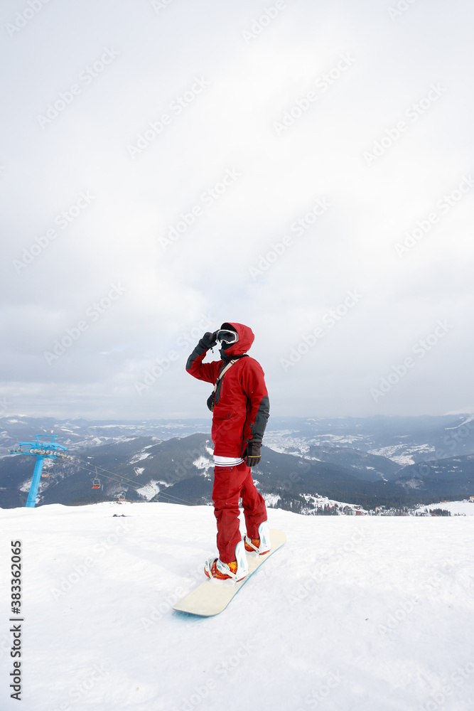 winter, leisure, sport and people concept - Close up low angle of a snowboarder standing on his board overlooking a ski run on the snowy slope below at a winter resort