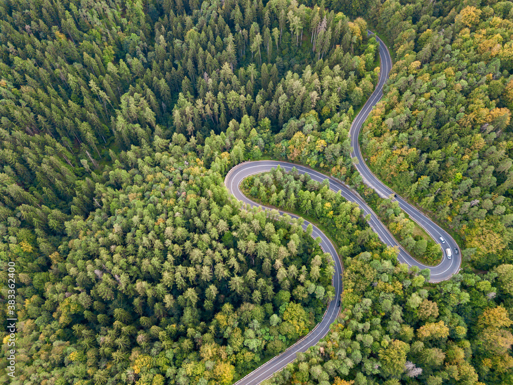 Winding road through the forest, from high mountain pass, in autumn season. Aerial view by drone. Romania