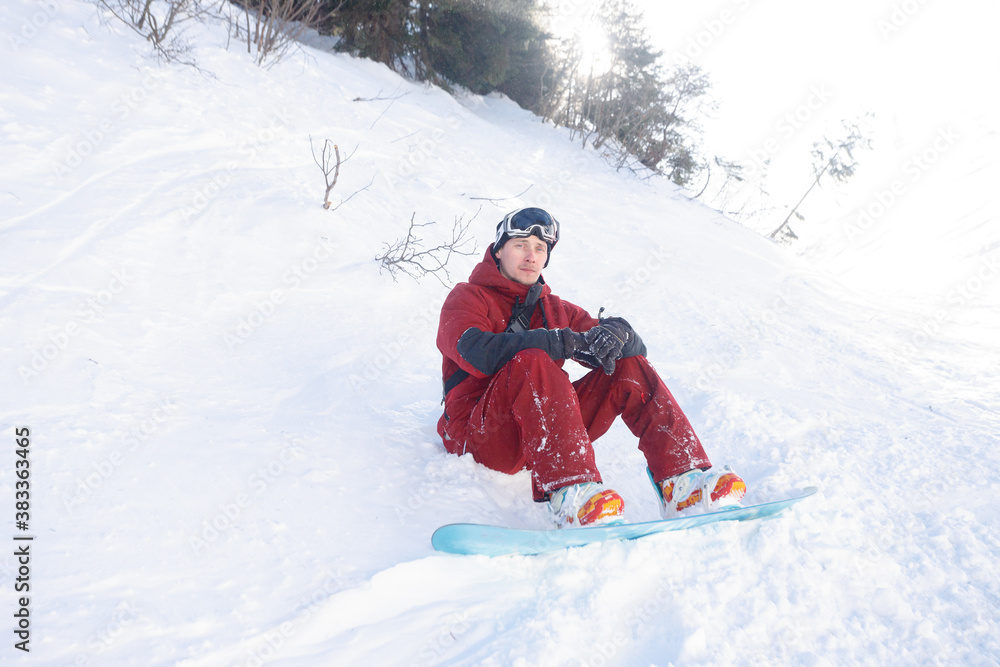 winter, leisure, sport and people concept - snowboarder sits high in the mountains on the edge of the slope and looks into the distance.