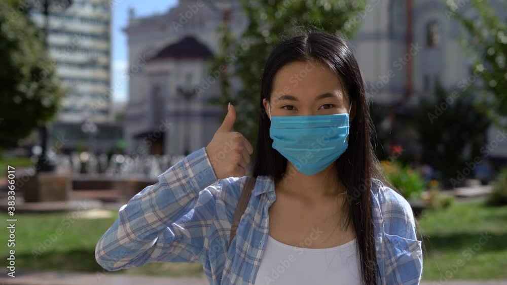 thumbs up gesture. young Asian woman in disposable protective mask shows like it. 4K thumbs up gesture. young Asian woman in disposable protective mask shows like it. 4K