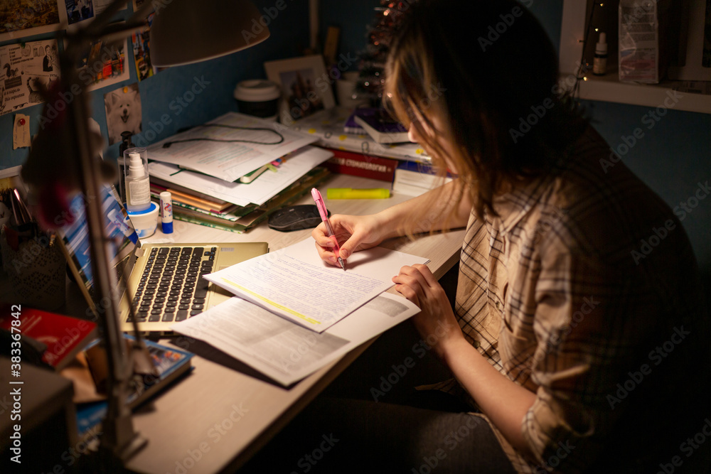 A girl is preparing for exams, writing at a table in the dark A girl is preparing for exams, writing at a table in the dark