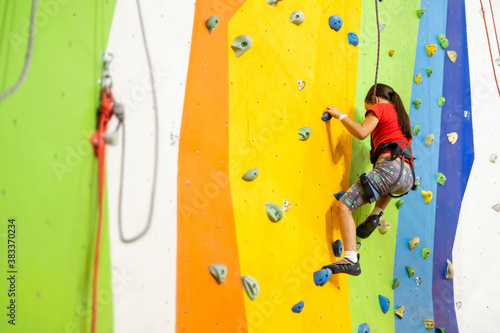 Sporty little girl climbing artificial boulder on practical wall in gym