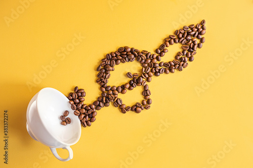 White cup and coffee beans forming the shape of a treble clef on a yellow background. Creative concept for coffee shops. Top view, copy space, minimalism, conceptual flat lay.