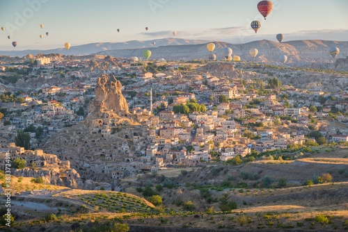 Bbaloons flying over Cappadocia landscape at sunrise with village photo