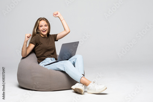 Young woman sitting on pufff with laptop with win gesture isolated on white background