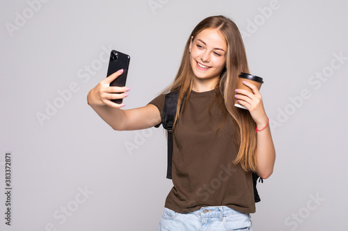 Portrait of a smiling attractive woman in suit taking a selfie while holding take away coffee cup over white background