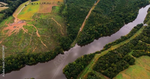 We fly across the the inlet for Lake Mackintosh in Whitsett, NC and see power distribution lines and pylons, clear cut wooded area with erosion, open fields and several warehouses. photo