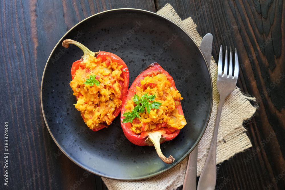 Homemade baked stuffed peppers filled with red lentils with vegetables on a dark plate, wooden background Homemade baked stuffed peppers filled with red lentils with vegetables on a dark plate, wooden background