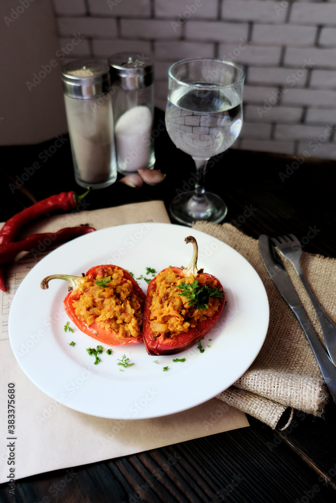 Homemade baked stuffed peppers filled with red lentils with vegetables on a white plate and glass of whater, wooden background