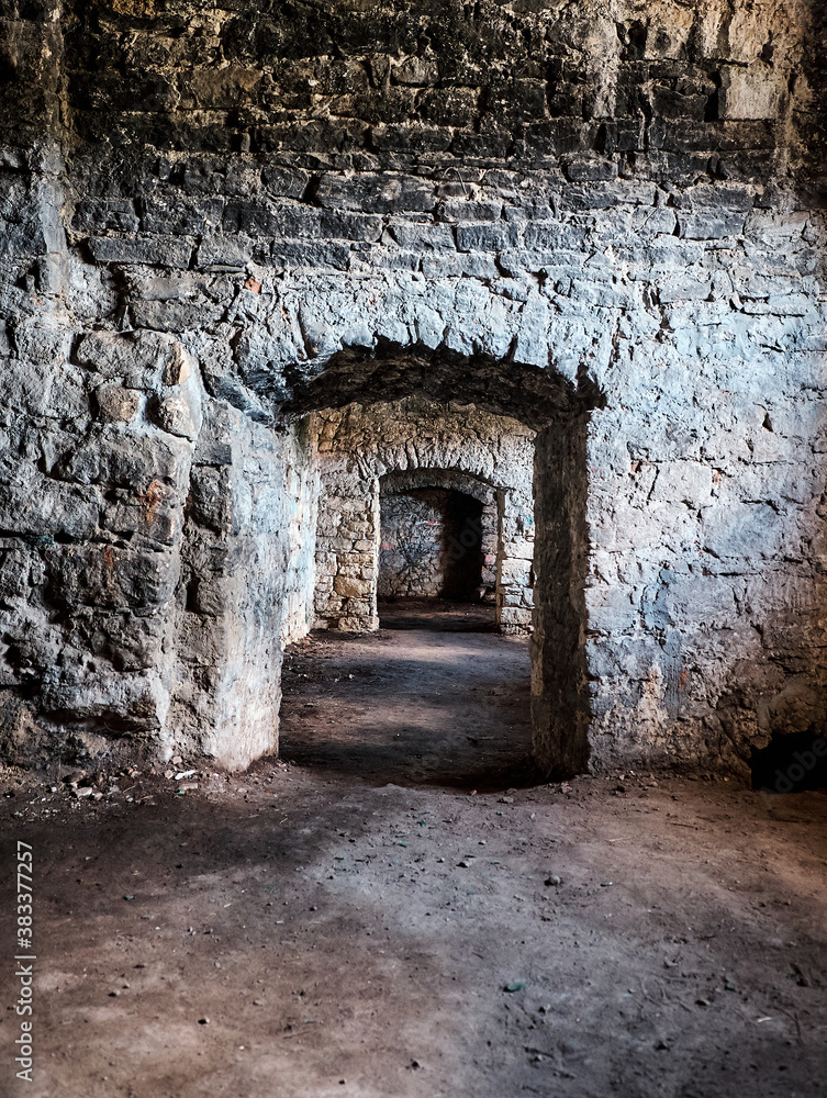 Ancient stone basement with arches. The sun breaks through  window. Long corridor through several rooms. Earthen floor.
