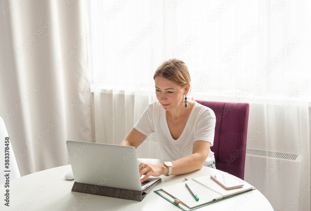 middle-aged woman works on a laptop at home in a light interior at a remote job middle-aged woman works on a laptop at home in a light interior at a remote job