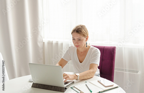 Free Download middle-aged woman works on a laptop at home in a light interior at a remote job - GFXLoad