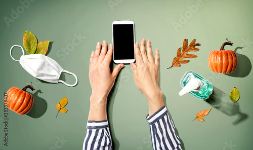 Smartphone with a mask and a sanitizer bottle in Autumn