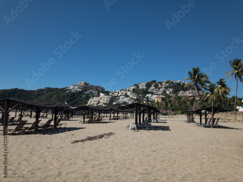 Camastros en playa de Acapulco. Al fondo cerro con viviendas.
