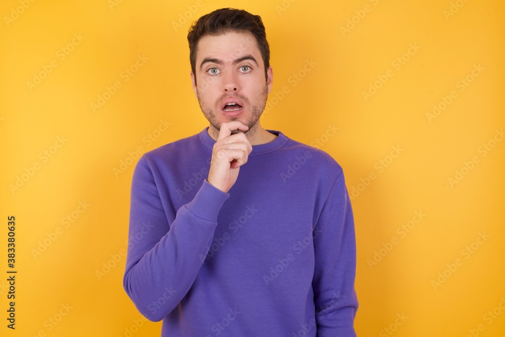 Nervous puzzled man Handsome man with sweatshirt over isolated yellow background opens mouth from surprise, reacts on sudden news. Nervous puzzled man Handsome man with sweatshirt over isolated yellow background opens mouth from surprise, reacts on sudden news.