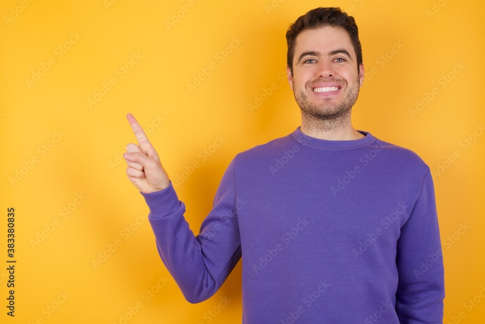 Handsome man with sweatshirt over isolated yellow background looking indicating fingers hands side empty space advising novelt Handsome man with sweatshirt over isolated yellow background looking indicating fingers hands side empty space advising novelt