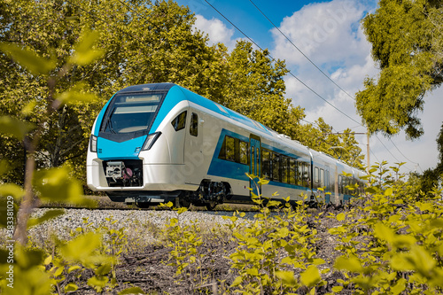 Modern and new passenger commuter Train in white and blue color is traveling on a single track railway line between the green leaves on an autumn day. photo