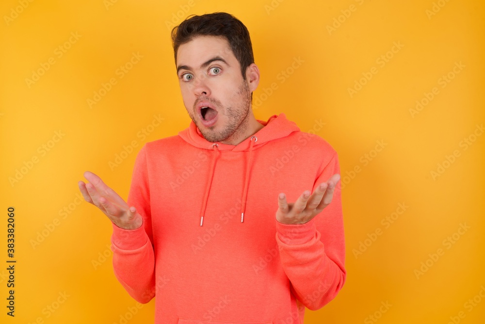 Frustrated Handsome man with sweatshirt over isolated yellow background feels puzzled and hesitant, shrugs shoulders in bewilderment, keeps mouth widely opened, doesn't know what to do. Frustrated Handsome man with sweatshirt over isolated yellow background feels puzzled and hesitant, shrugs shoulders in bewilderment, keeps mouth widely opened, doesn't know what to do.