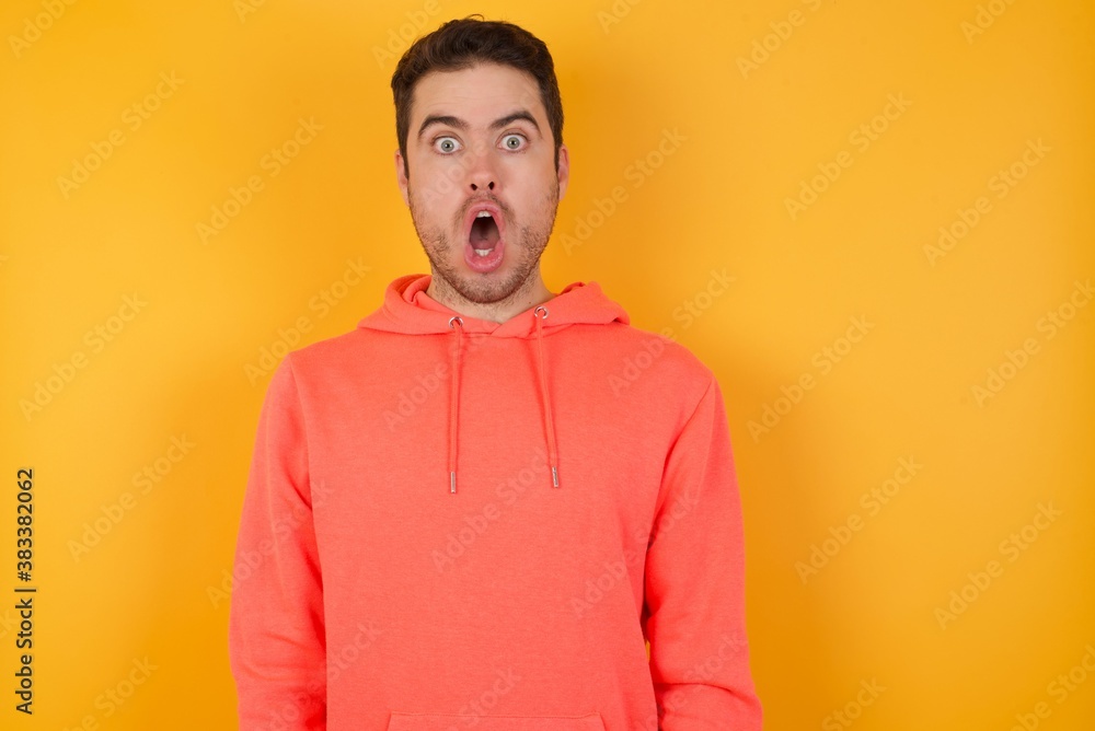 Oh my God. Surprised Handsome man with sweatshirt over isolated yellow background stares at camera with shocked expression exclaims with unexpectedness, Oh my God. Surprised Handsome man with sweatshirt over isolated yellow background stares at camera with shocked expression exclaims with unexpectedness,