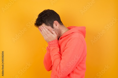 Sad Handsome man with sweatshirt over isolated yellow background crying covering his face with his  hands. © Roquillo